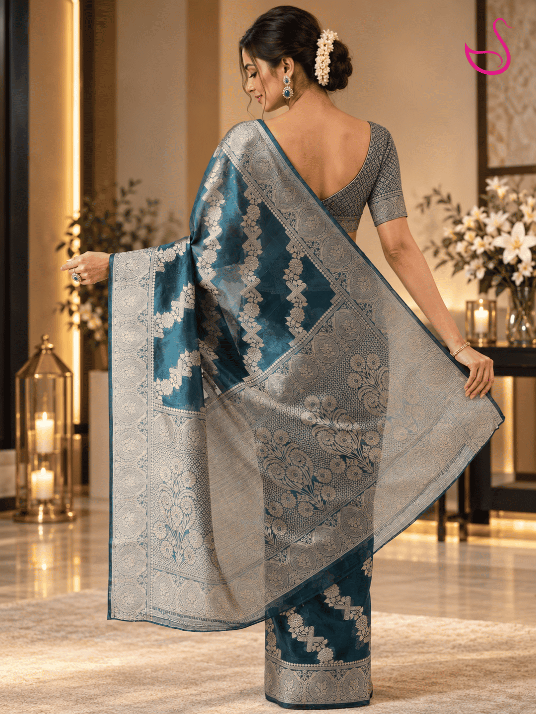 Back view of a model wearing a deep teal blue Banarasi saree showcasing its intricate silver floral weave, detailed zari border and richly patterned pallu, paired with a statement blouse.