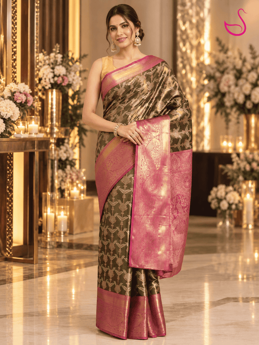 Elegant woman wearing a dark olive-green and pink-gold brocade saree with an ornate zari pallu, posed in a luxurious reception setting with warm lighting, floral décor and candles. Ishaana Ethnics emblem appears in the top-right corner.