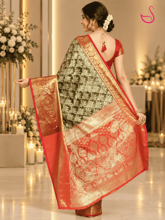 woman shown from the back wearing an black tissue silk saree with intricate gold motifs and an elaborate red-orange and gold zari pallu, paired with a red blouse and traditional jewellery, highlighting the saree’s detailed pallu design.