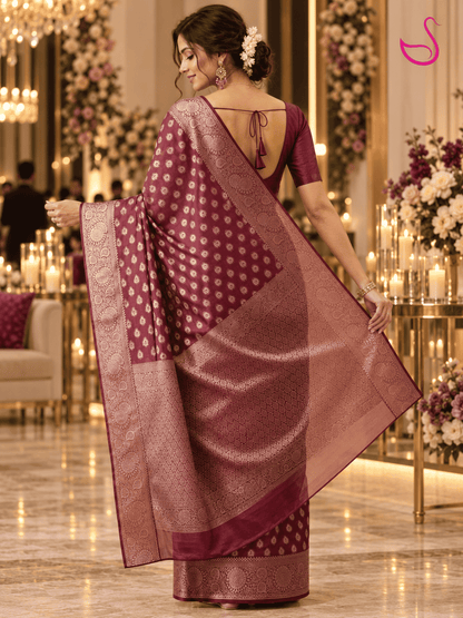 Maroon woven saree blouse with intricate all-over traditional motifs, short sleeves, a deep V-shaped back neckline and detailed patterned borders, displayed against a dark interior background.